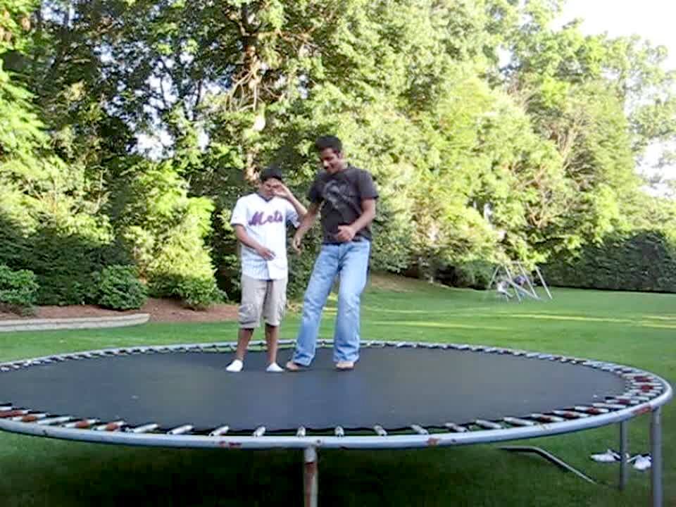 Video thumbnail showing: 2 young men are on a trampoline. 1 jumps and flies off the trampoline. He laughs when he hits the ground.