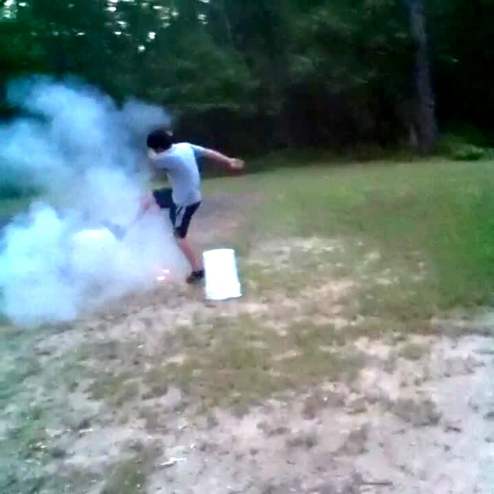 Video thumbnail showing: A young boy lights a firework then puts a bucket over it and sits on it. The bucket explodes and he runs away. The boy was not harmed.
